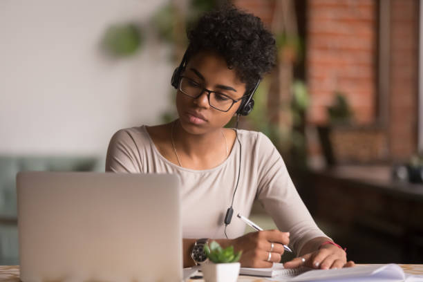 Focused mixed race woman wearing headphones watching a webinar online on her laptop listening to the lecture